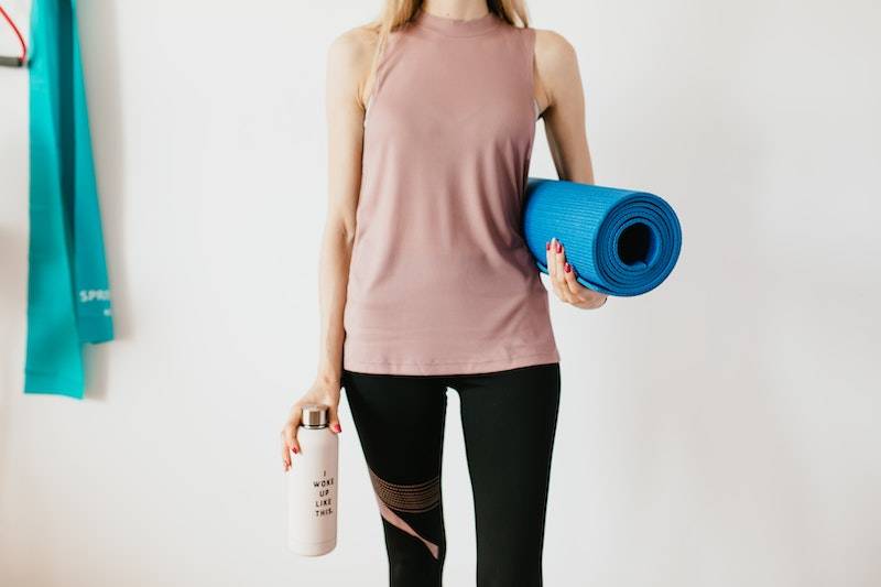 woman holding yoga mat and water bottle