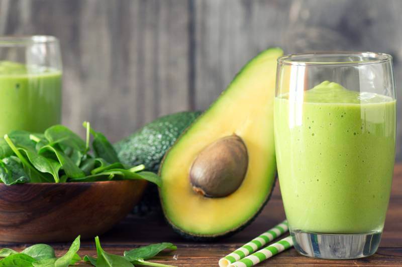 avocado fruit sliced in half with smoothie in a glass