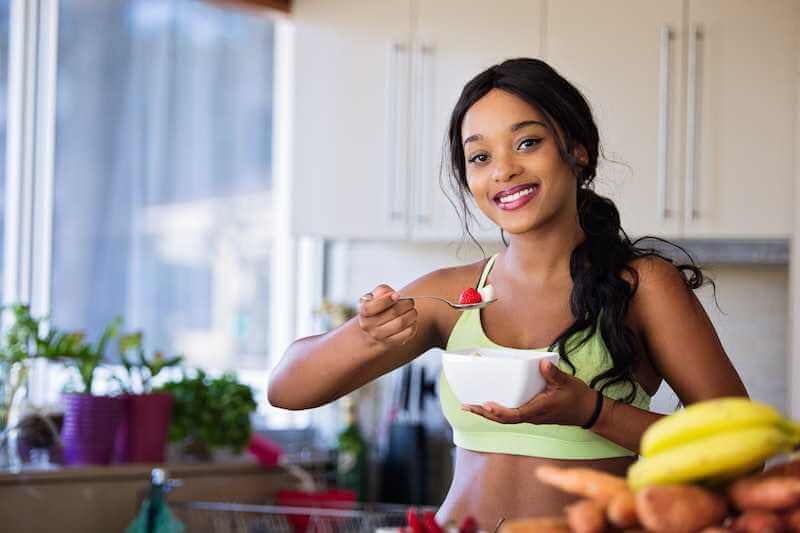 smiling woman holding a spoon and bowl of fresh fruits