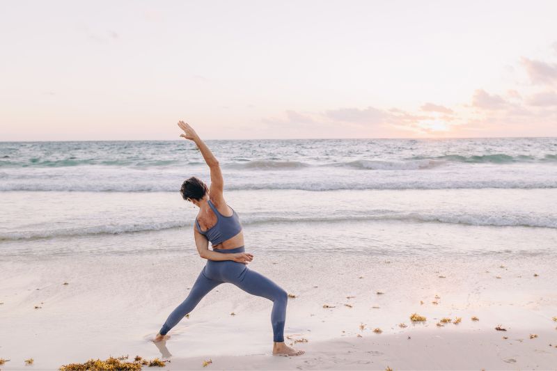 aged woman in a beach stretching in front of a small waves