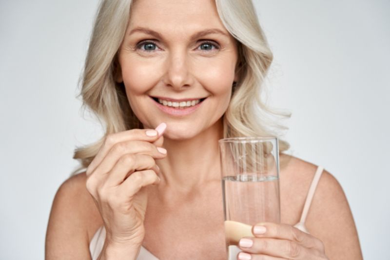 aged woman holding a pink pill and a glass