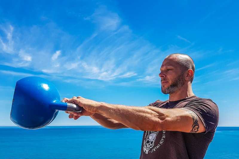 man using the kettlebell outdoors with blue sky