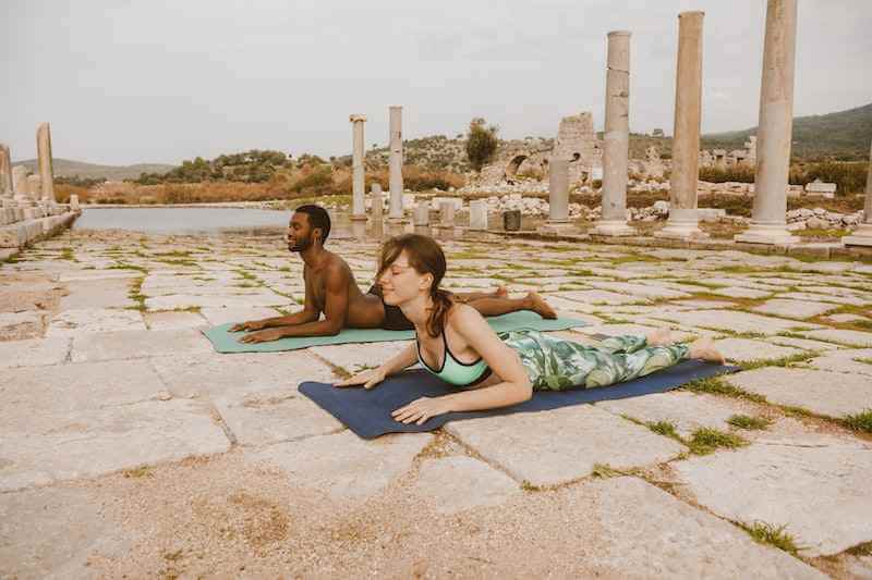 man and woman doing a sphinx pose yoga outdoors