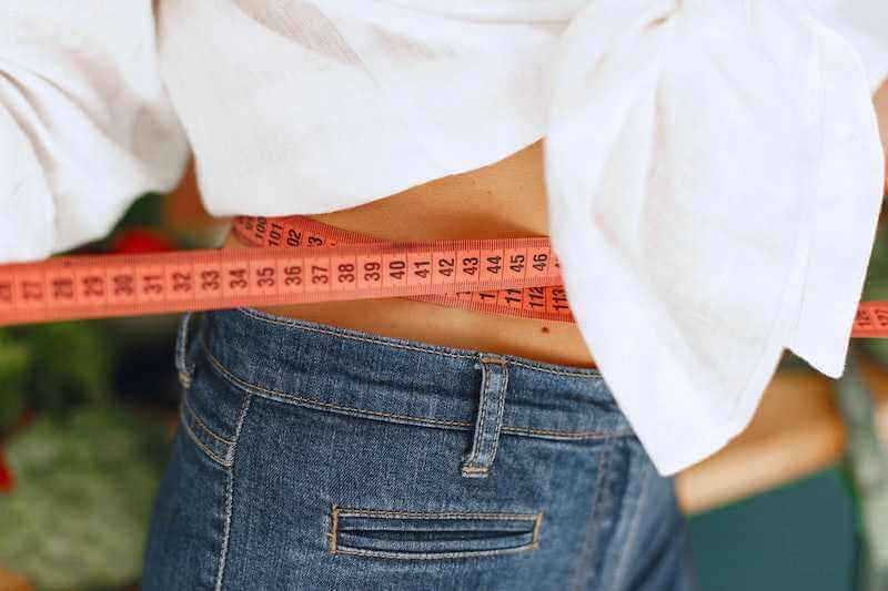 woman in white cropped top measuring waist