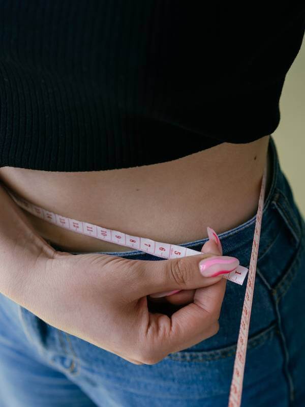 woman in black cropped top measuring her waist with tape measure